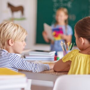 Two children sitting at a table with notebooks and colored pencils.