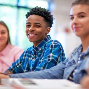 Three students smiling while working together in a classroom.