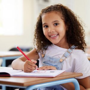 A smiling girl with curly hair, wearing a white shirt and denim overalls
