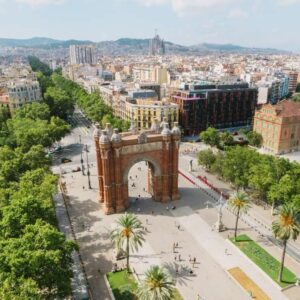 Aerial view of Arc de Triomf in Barcelona with surrounding tree-lined promenade and cityscape background