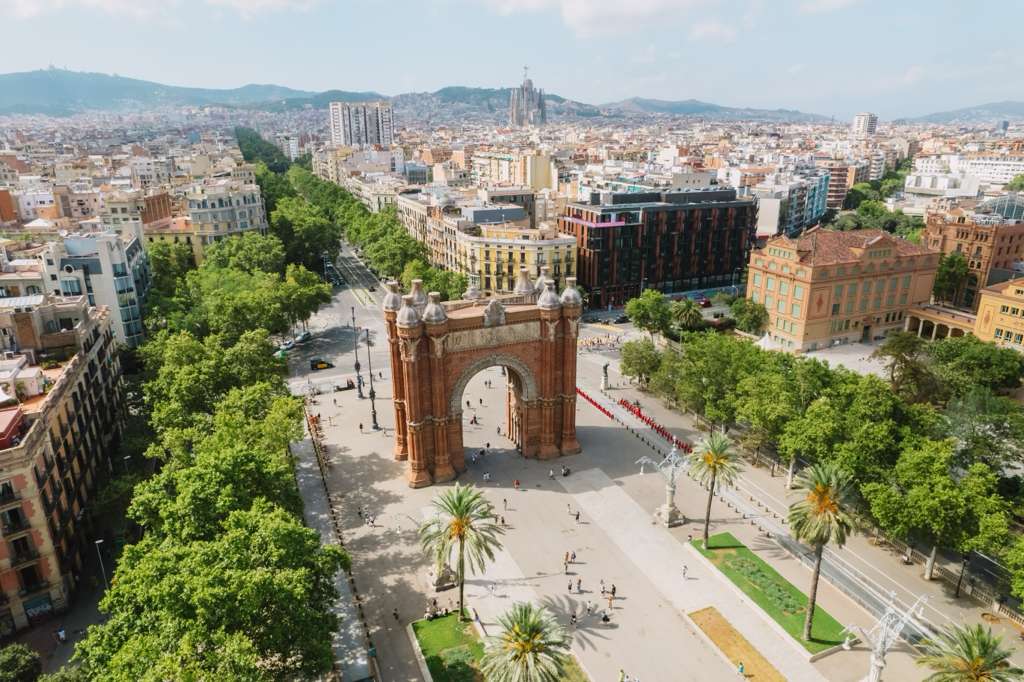 Aerial view of Arc de Triomf in Barcelona with surrounding tree-lined promenade and cityscape background